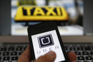 An illustration picture shows the logo of car-sharing service app Uber on a smartphone next to the picture of an official German taxi sign in Frankfurt, September 15, 2014. A Frankfurt high court will hold a hearing on a recent lawsuit brought against Uberpop by Taxi Deutschland on Tuesday.  San Francisco-based Uber, which allows users to summon taxi-like services on their smartphones, offers two main services, Uber, its classic low-cost, limousine pick-up service, and Uberpop, a newer ride-sharing service, which connects private drivers to passengers - an established practice in Germany that nonetheless operates in a legal grey area of rules governing commercial transportation. The company has faced regulatory scrutiny and court injunctions from its early days, even as it has expanded rapidly into roughly 150 cities around the world.   REUTERS/Kai Pfaffenbach (GERMANY - Tags: BUSINESS EMPLOYMENT CRIME LAW TRANSPORT)